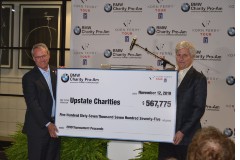 Max Metcalf, left, and Bob Stegner unveil and present a check representing the funds to be divided among four charities from the 2019 tournament. (Photo/Ross Norton)