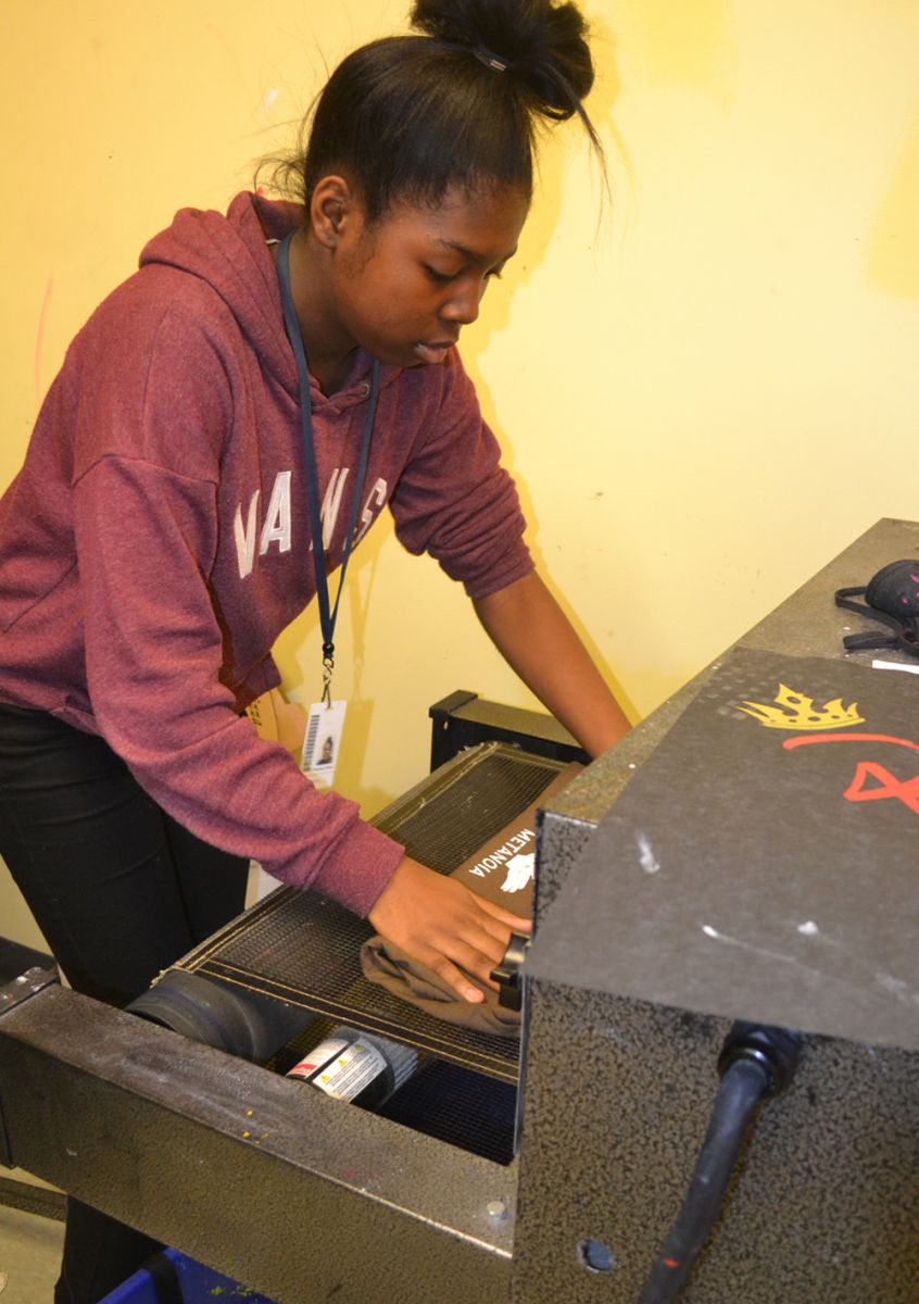 Princess Fisher, a freshman, places a T-shirt onto a conveyor belt, which goes into a drying machine. The newly printed designs dry within a few minutes. (Photo/Liz Segrist)