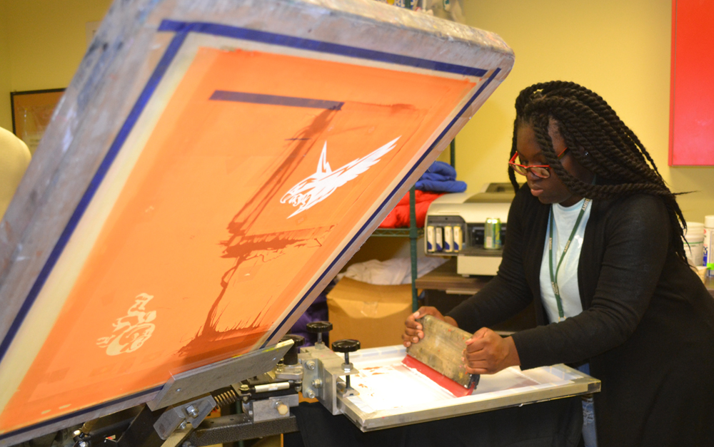 Tonisha Forrest, a ninth-grader, works on a screen press for Hodari Screen Printing along Reynolds Avenue in North Charleston. Students fulfill orders on the press, spreading ink across designs and imprinting them onto T-shirts for customers. (Photo/Liz Segrist)