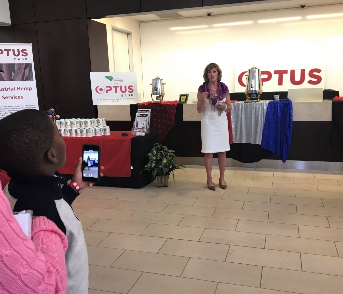 A child films a video of Kat Taylor, co-founder and CEO of Oakland, Calif.-based Beneficial State Bank and wife of Democratic presidential candidate Tom Steyer, as she speaks at Optus Bank on Monday. (Photo/Melinda Waldrop) 